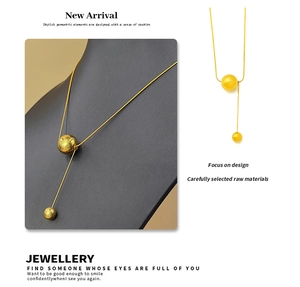 Detailopname van een gouden titanium halsketting met twee bollen en asymmetrisch design