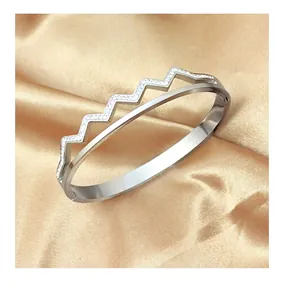 Macro shot of silver wavy stainless steel bangle with pavé zircons on satin background