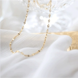 Detailed view of an 18k gold lip-shaped link chain necklace on soft white fabric background