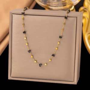 Détail du collier en acier doré avec perles triangles noires sur présentoir brun