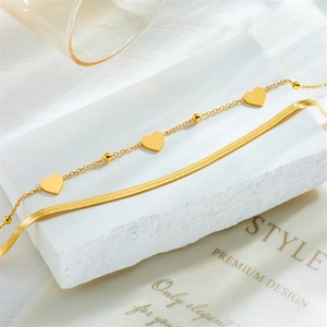 Gold double-layered anklet set with snake chain and heart pendant on a stone