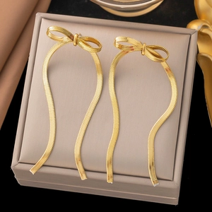 Golden bow stud earrings with long snake chain tassels on a beige jewelry box