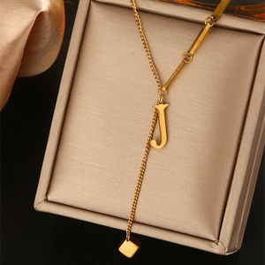 Detailopname van gouden Y-vormige ketting met letter J hanger op luxe satijnen stof