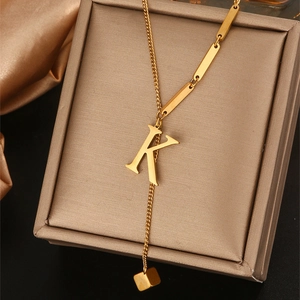 Detail van gouden ketting met hanger letter K en metalen staaf op sieradendoos