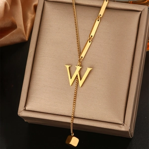 Detail van gouden letter W kwastje ketting met asymmetrische ketting en hanger