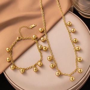Titanium steel necklace and bracelet set with polished gold bead pendants on silk background