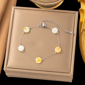 Detail of a thin silver bracelet with colorful shell charms on a gold silk jewelry box