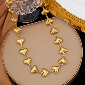Elegante collana dorata con elementi a cuore 3D collegati su un piedistallo neutro