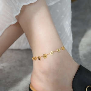 Detail shot of a golden daisy anklet with 3D flower charms worn with a white lace dress