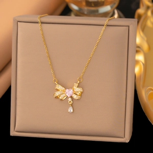 Detail einer goldenen Schleifenkette mit rosa Herzstein und tropfenförmigem Anhänger