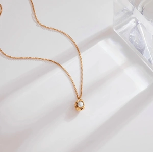 Dettaglio macro del ciondolo con perla d'acqua dolce, montatura a spirale dorata