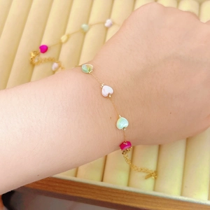 Dettaglio di un bracciale dorato con ciondoli a cuore colorati su vassoio in velluto beige