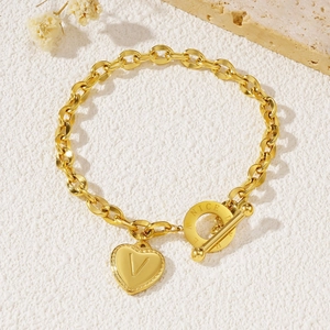 Gold OT clasp heart pendant bracelet with letter V engraving on textured white background