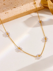 Detail of 18k gold chain with five white pearl daisy charms on textured stone