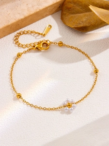 Detail of 18k gold beaded chain necklace with pearl flower pendant on white textured stone