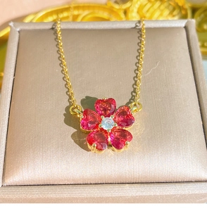Dettaglio macro dei petali di zircone rosso a cuore e diamante sulla collana dorata