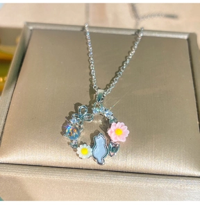 Dettaglio del ciondolo a ghirlanda con gattino, fiori rosa e cristallo blu su catena