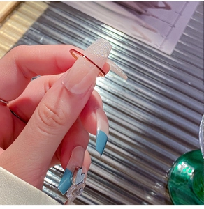 Vista macro de uñas de bailarina largas con puntas azules y dijes de corazón plata