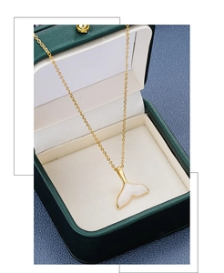 Detail of a gold-plated fishtail necklace with white enamel in a green jewelry box
