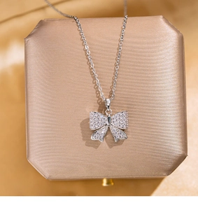 Détail du pendentif nœud argenté avec cristaux pavés sur boîte en satin doré