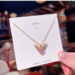 Detail of pink heart crystal necklace with golden antler design on a white display card