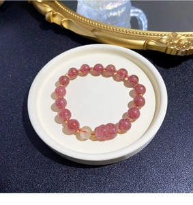 Detail of pink strawberry quartz bracelet with golden beads and a carved piyao charm