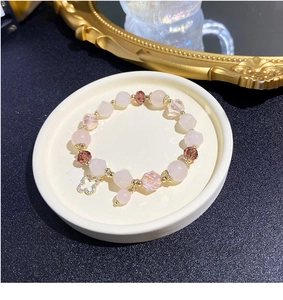 Detail of beaded bracelet with pink strawberry quartz and a golden clover charm