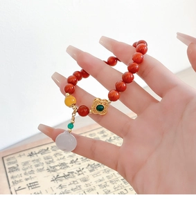 Detail of beaded natural stone bracelet with red cinnabar beads and floral pendant