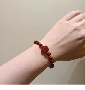 Detailed shot of red cinnabar bead bracelet featuring a golden plum blossom charm on wrist