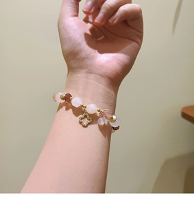 Macro detail of natural pink stone beaded bracelet featuring a gold clover pendant