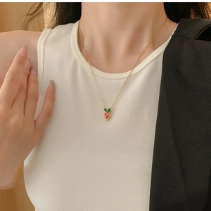 Detail of creative carrot pendant with red and green gemstones on golden necklace