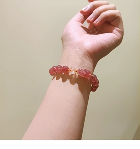 Close-up of a natural pink strawberry quartz beaded bracelet with a carved charm charm