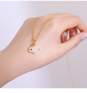 Detail van een gouden titanium ketting met wit konijn-hangertje en rood edelsteenoogje