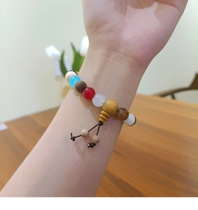 Detail of multi-color gemstone beads bracelet with a yellow wooden charm on wrist