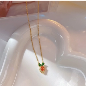 Detailed view of carrot pendant with orange stone and green leaves on a heart plate