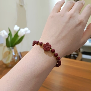 Natural cinnabar stone bead bracelet with flower charm and gold spacers on a wrist