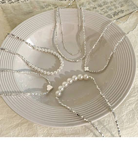 Gros plan d'un collier de perles et billes d'argent avec breloques cœur et trèfle