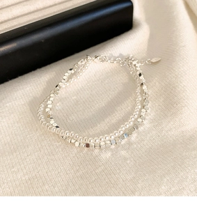 Detailaufnahme eines zweilagigen Armbands mit weißen Perlen und silbernen Metallwürfeln