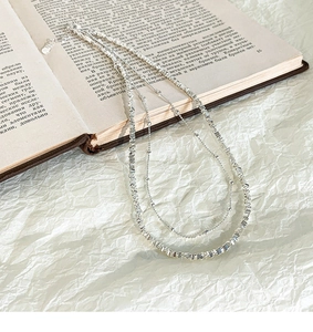Détail du collier argenté multicouche posé élégamment sur un livre vintage de style français