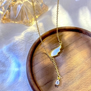 Goldene Engelsflügel-Halskette mit Zirkonia-Tropfen auf edlem Holztablett
