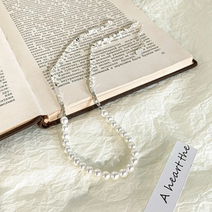 Dettaglio collana di perle e sfere argentate con ciondolo a cuore su libro vintage