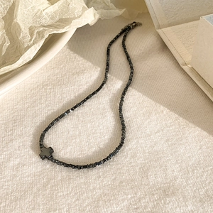 Dettaglio di una collana minimalista in ematite nera con un piccolo ciondolo a croce