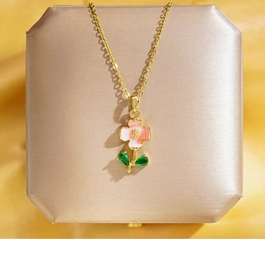 Dettaglio del ciondolo a fiore rosa con pietre verdi su raso color champagne