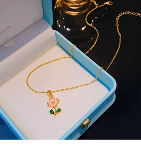 Dettaglio collana in oro 18 carati con fiori rosa e foglie verdi su scatola portagioielli