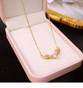 Vista detallada de collar de cuernos de ciervo dorado con circón de corazón en caja rosa