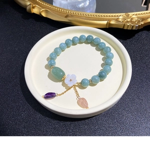 Detalle de pulsera de cuentas verdes con dije de flor de concha en bandeja de cerámica