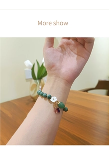 Detalle de una pulsera de cuentas con piedras verdes y colgante de flor de concha blanca