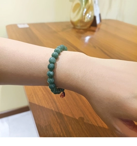 Detalle de pulsera de cuentas de piedra verde oscuro con colgante de gota púrpura en la muñeca