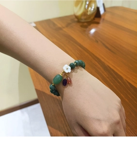 Detalle de la pulsera de cuentas verde oscuro con flores y colgantes de colores en la muñeca