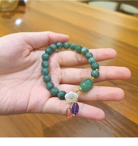 Detalle de pulsera de cuentas de jade verde con dije de flor en la muñeca de mujer